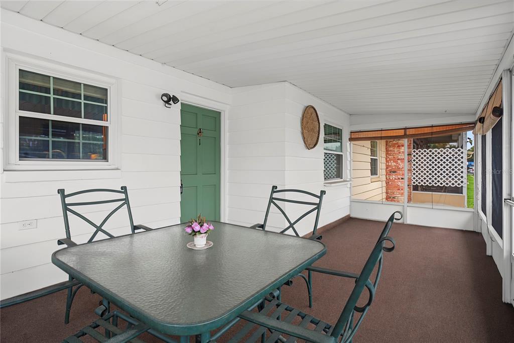 A covered patio features a glass-topped table, metal chairs, and a green exterior door — 1001 PLANTATION DRIVE UNIT C1, KISSIMMEE, FL