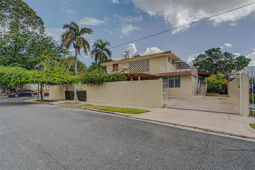 A two-story beige house with a concrete wall, palm trees, and a paved driveway — 901 HARVARD, SAN JUAN, PR