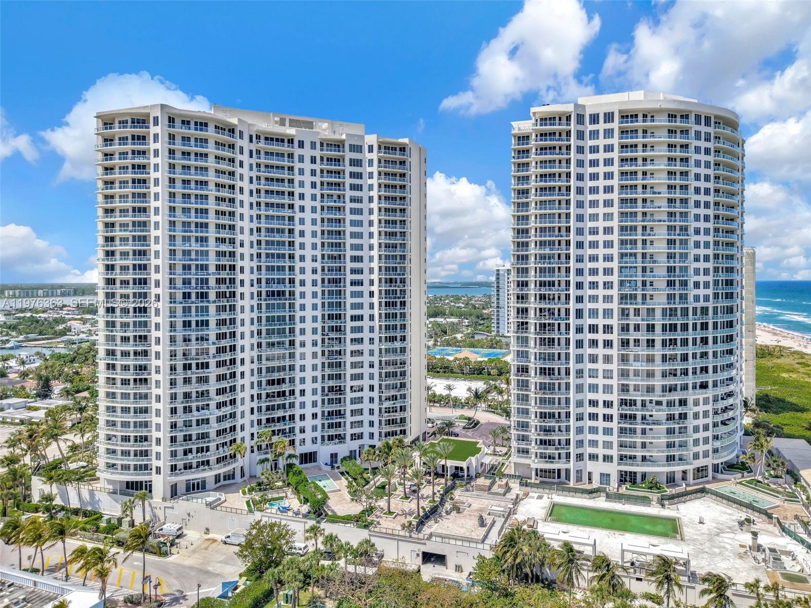 Two tall, white residential high-rise buildings stand near a beach under a blue sky — 2700 N Ocean Drive # 902B, Singer Island FL 33404, SINGER ISLAND, FL
