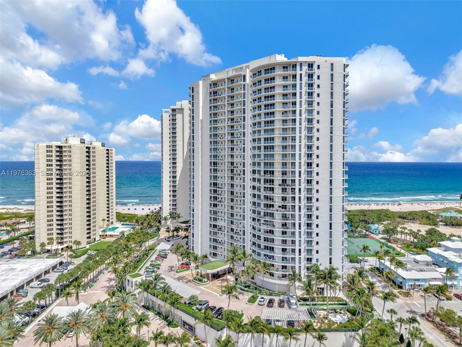 An aerial view shows two tall white residential towers situated along a sandy beach — 2700 N Ocean Drive # 902B, Singer Island FL 33404, SINGER ISLAND, FL