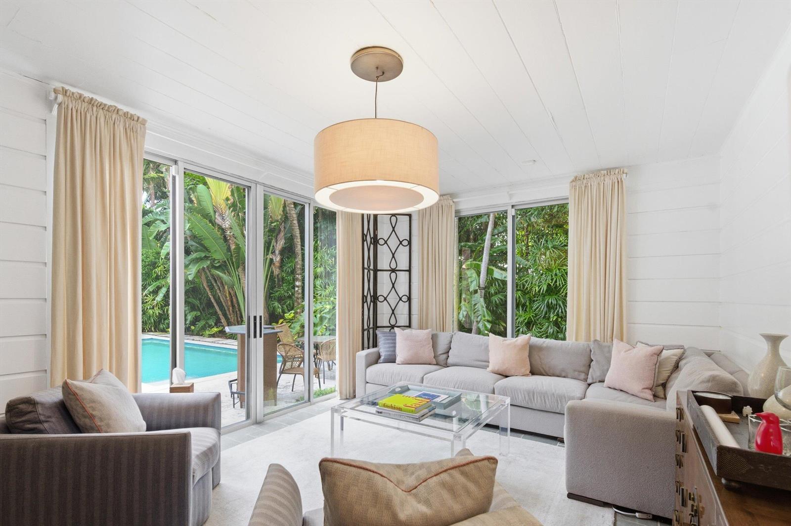 A living room with a gray sectional, glass coffee table, and sliding doors overlooking a pool — 258 Pendleton Avenue, Palm Beach FL 33480, PALM BEACH, FL