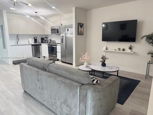 A modern open-concept living room and kitchen featuring light wood floors and stainless steel appliances — 19380 NE 26th Ave # 304, Miami FL 33180, MIAMI, FL