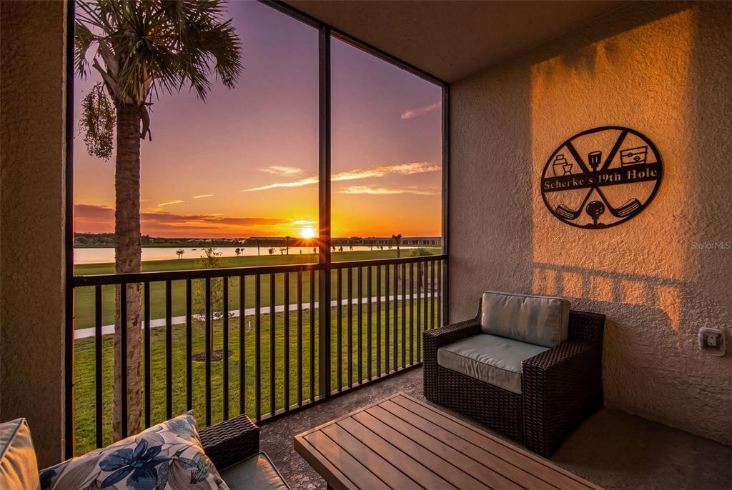A screened-in balcony features wicker furniture, a wooden table, and a sunset view of a golf course — 15275 GREEN ACRES AVENUE UNIT 321, PUNTA GORDA, FL