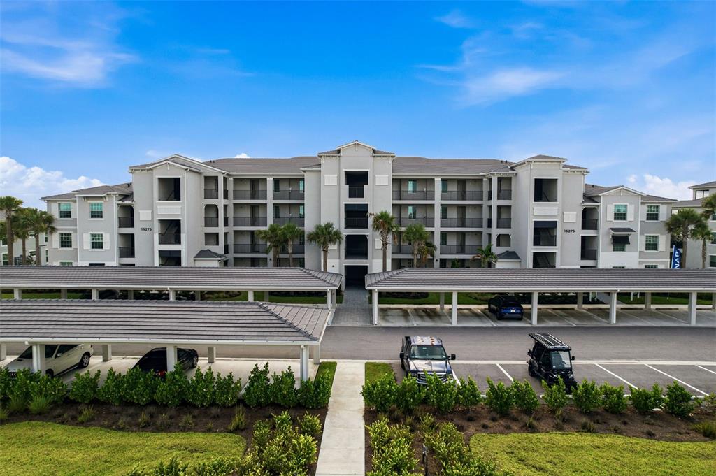 An exterior view of a multi-story apartment building with covered parking structures in the foreground — 15275 GREEN ACRES AVENUE UNIT 321, PUNTA GORDA, FL