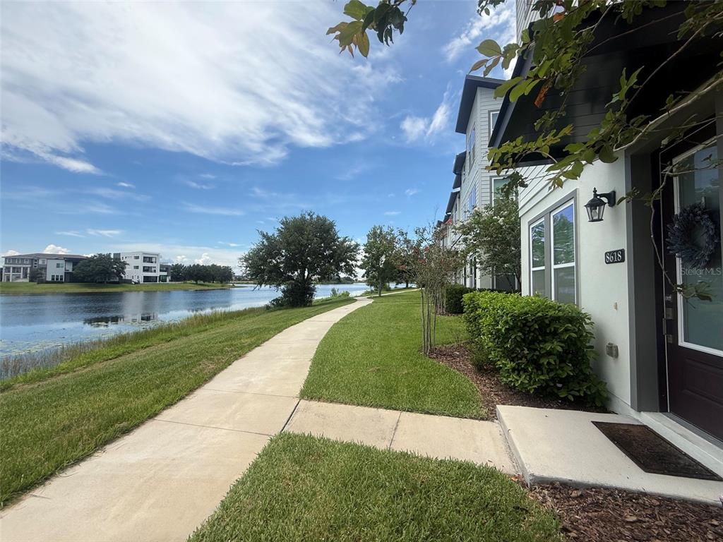 A concrete walkway runs along a grassy lawn beside a lake and apartment buildings — 8618 WARBURG ALLEY, ORLANDO, FL