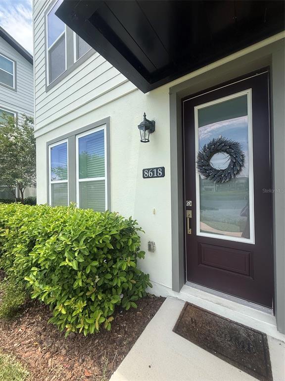 A dark front door with a wreath and a house number sits beside a green hedge — 8618 WARBURG ALLEY, ORLANDO, FL