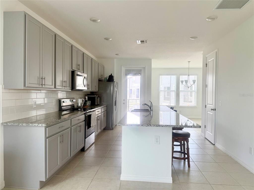 A kitchen features gray cabinets, granite countertops, a central island, and tile flooring — 8618 WARBURG ALLEY, ORLANDO, FL