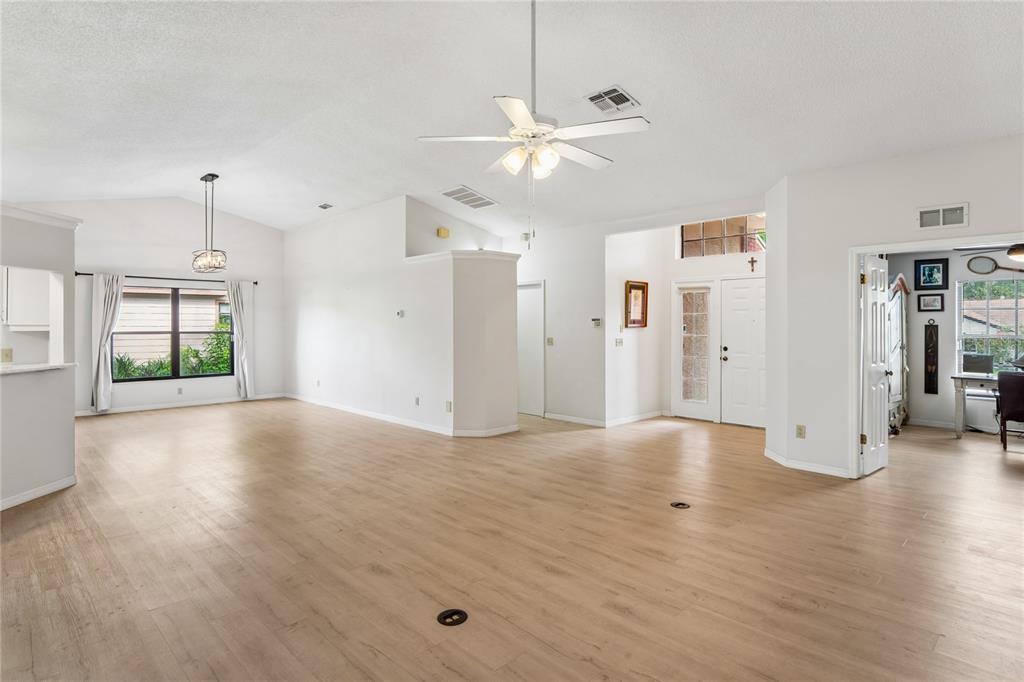 A spacious, open-concept living area features light wood-look flooring, a ceiling fan, and white walls — 8050 EACON COURT, HUDSON, FL
