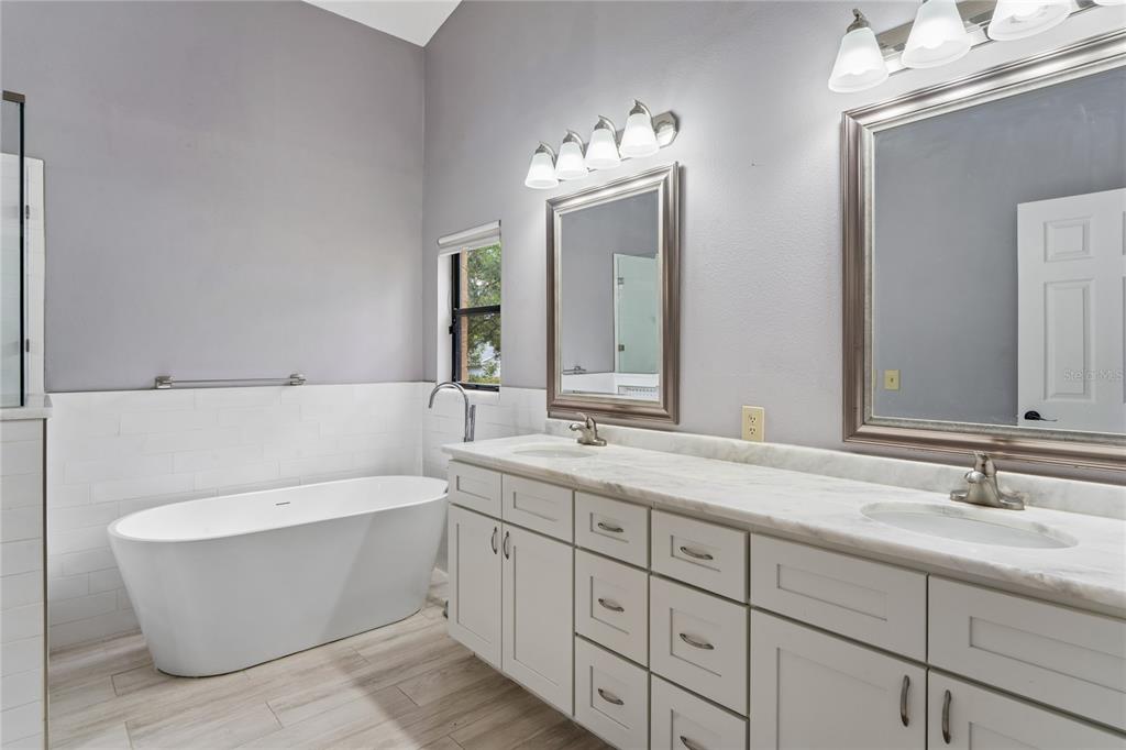 A bathroom features a freestanding tub, a double vanity with marble countertops, and two mirrors — 8050 EACON COURT, HUDSON, FL
