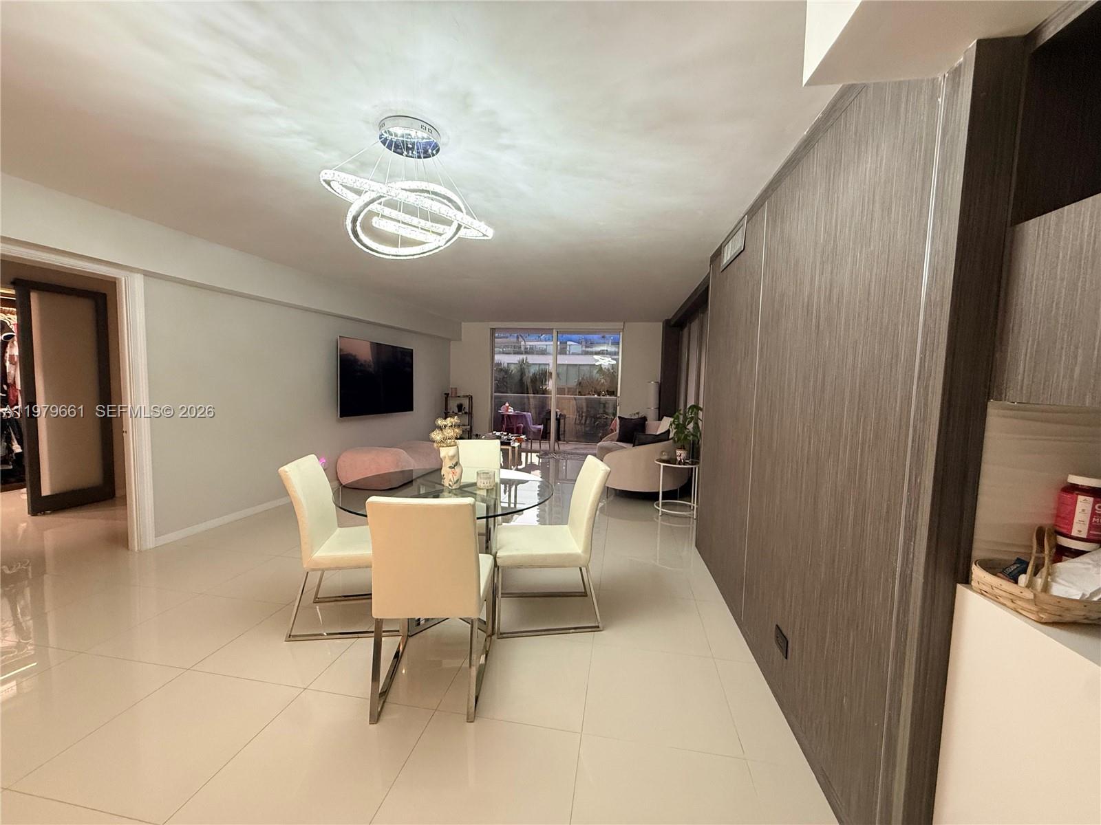 A dining area with a glass table and modern chandelier sits in an open-plan living space — 6039 Collins Ave # 635, Miami Beach FL 33140, MIAMI BEACH, FL
