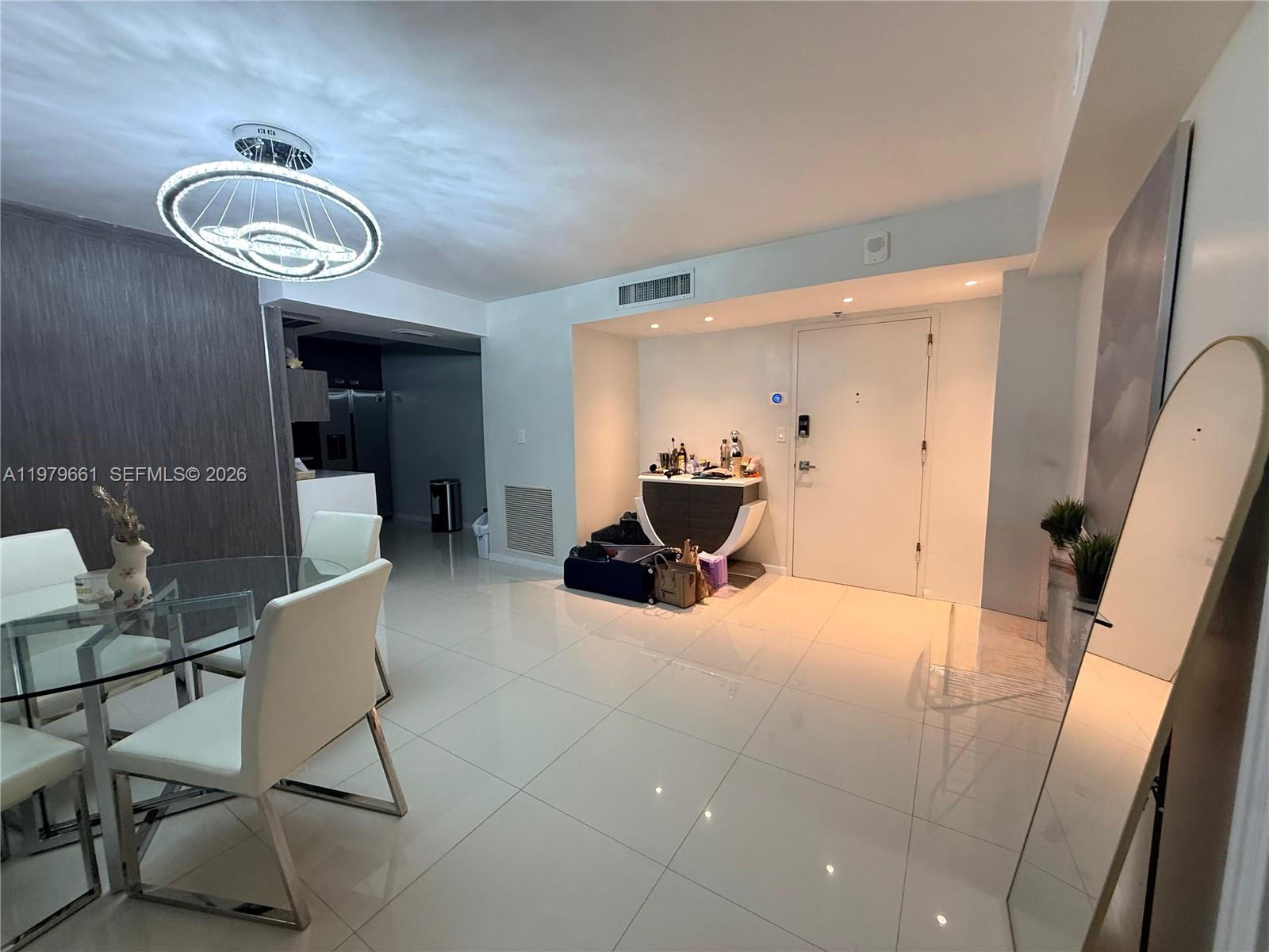 A dining area with a glass table and modern chandelier leads to an entryway — 6039 Collins Ave # 635, Miami Beach FL 33140, MIAMI BEACH, FL