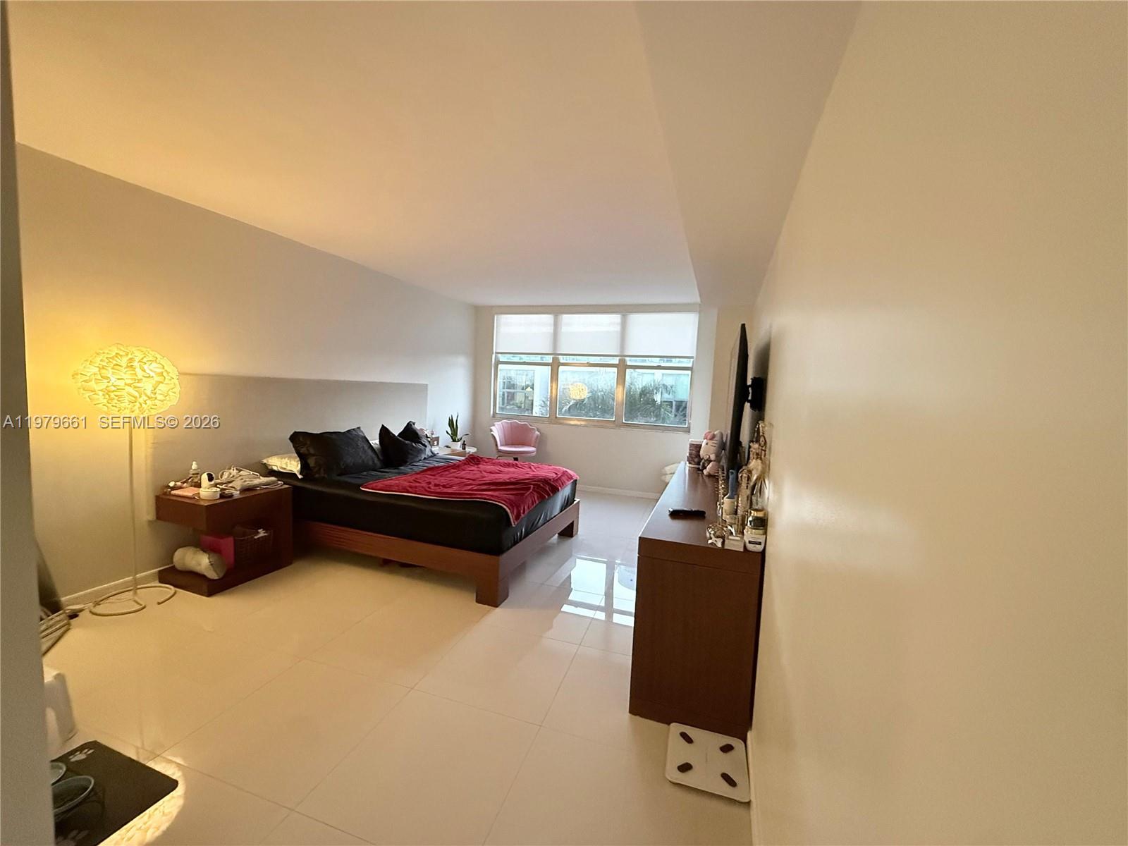 A bedroom features a platform bed, a wooden dresser, and large windows with white blinds — 6039 Collins Ave # 635, Miami Beach FL 33140, MIAMI BEACH, FL
