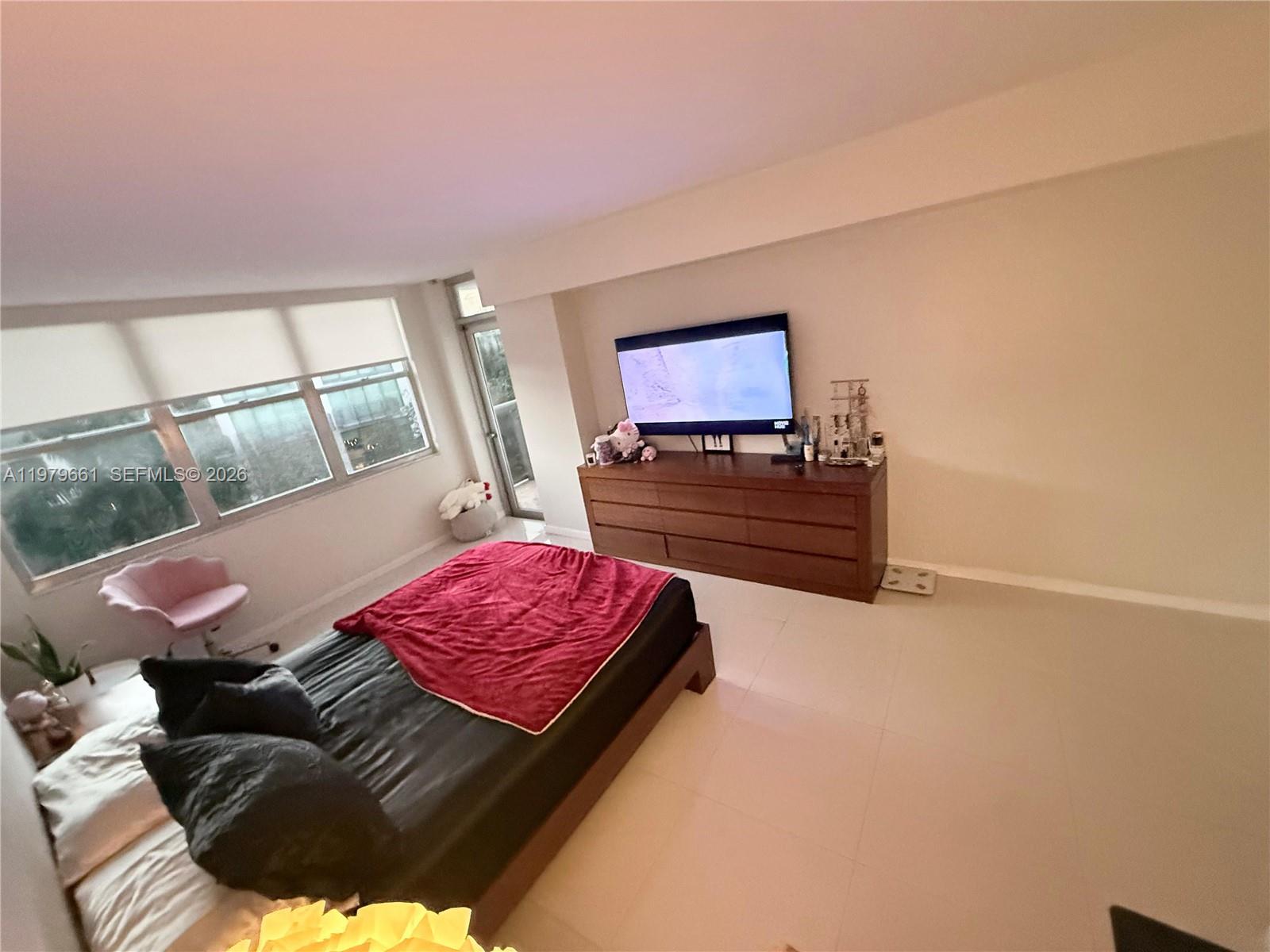 A bedroom features a bed with a red blanket, a wooden dresser, and large windows — 6039 Collins Ave # 635, Miami Beach FL 33140, MIAMI BEACH, FL