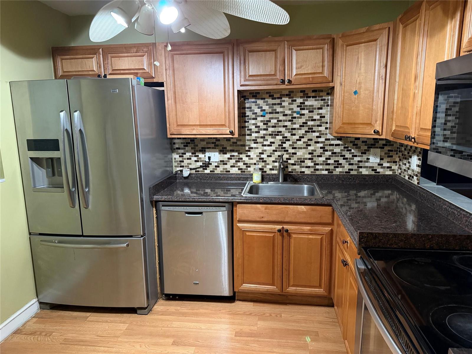 A kitchen features wood cabinets, stainless steel appliances, a mosaic tile backsplash, and dark countertops — 3110 Holiday Springs Boulevard # 108, Margate FL 33063, MARGATE, FL