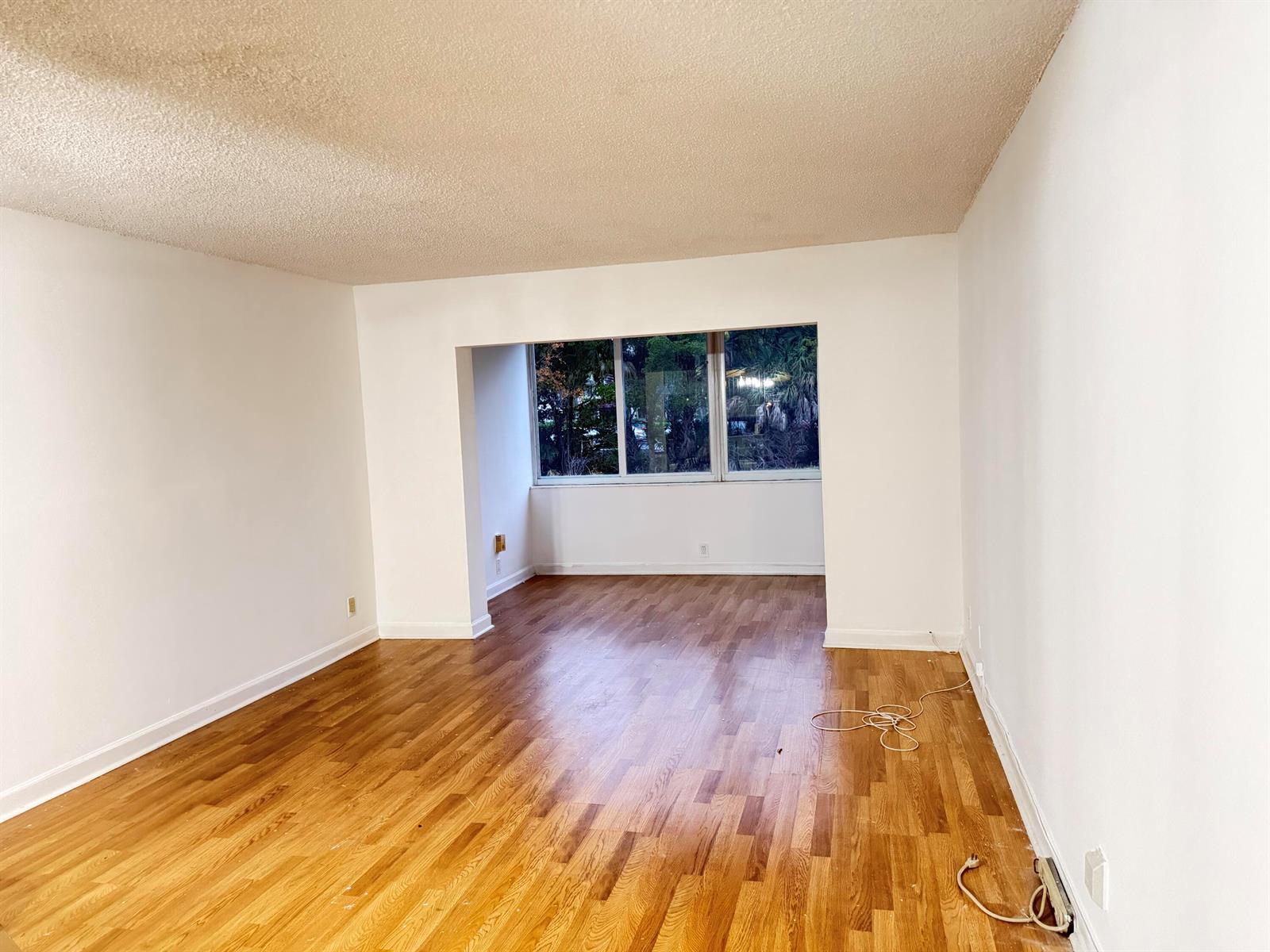 An empty room with hardwood floors, white walls, a popcorn ceiling, and a large window — 3110 Holiday Springs Boulevard # 108, Margate FL 33063, MARGATE, FL