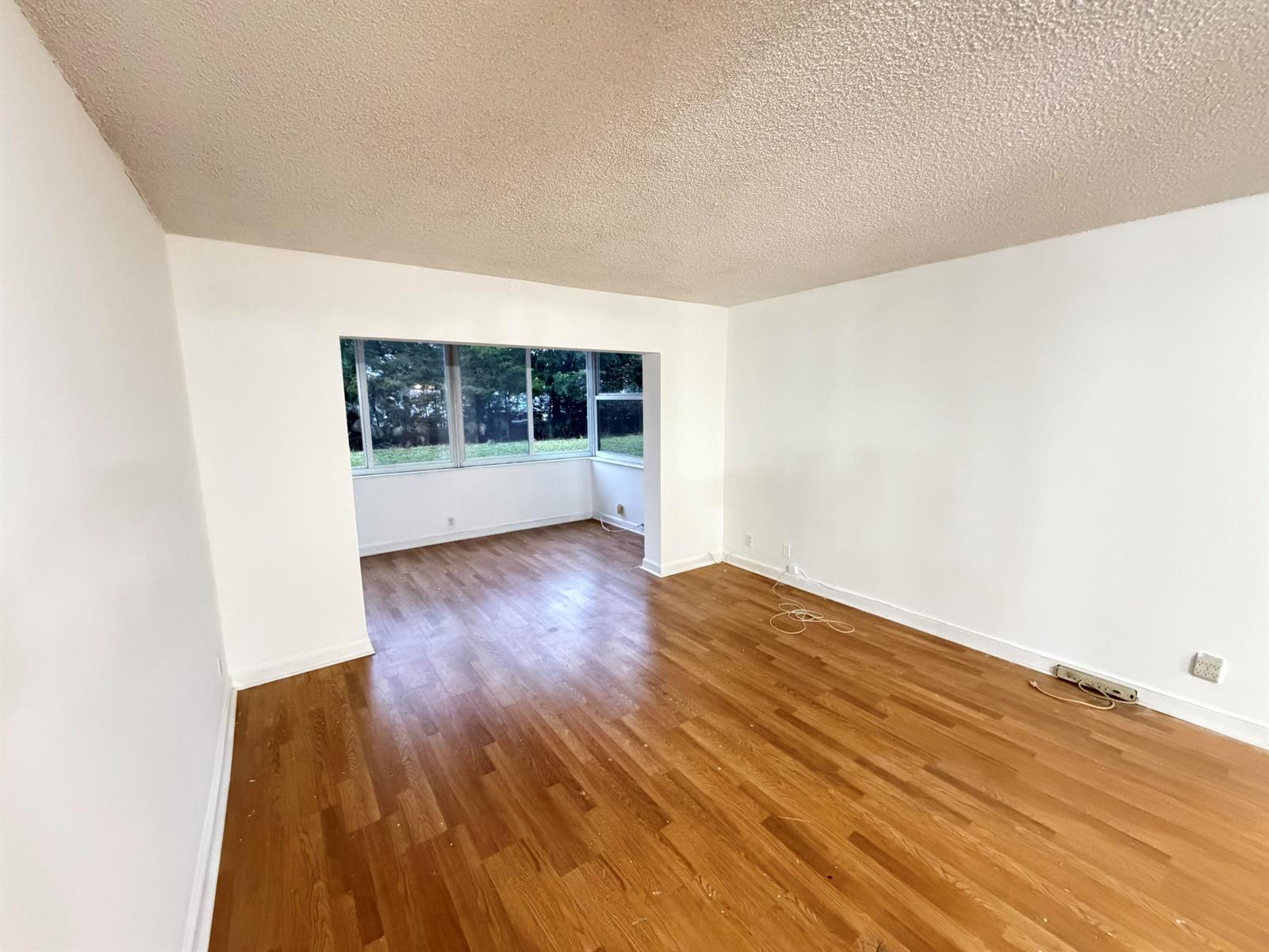 An empty room with wood-look flooring, white walls, a popcorn ceiling, and a large window — 3110 Holiday Springs Boulevard # 108, Margate FL 33063, MARGATE, FL