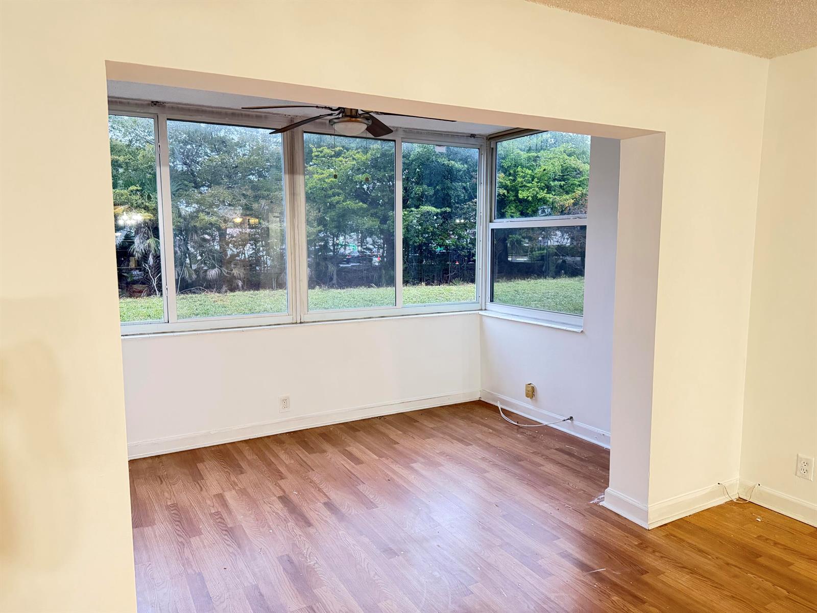 A sunroom with wood-look flooring and large windows overlooking a grassy yard and trees — 3110 Holiday Springs Boulevard # 108, Margate FL 33063, MARGATE, FL