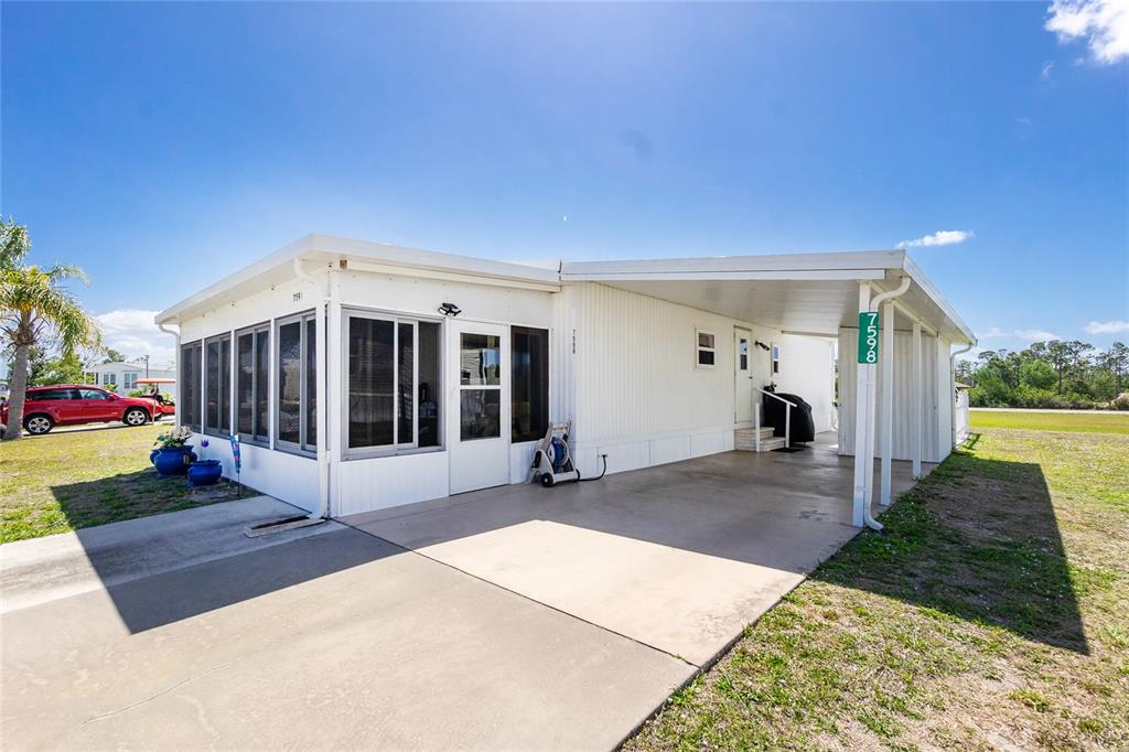 A white mobile home features a screened-in porch, a concrete driveway, and a covered carport — 7598 RATAN CIRCLE, PORT CHARLOTTE, FL