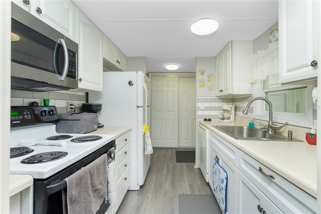 A galley kitchen features white cabinets, stainless steel appliances, a tile backsplash, and light flooring — 7598 RATAN CIRCLE, PORT CHARLOTTE, FL