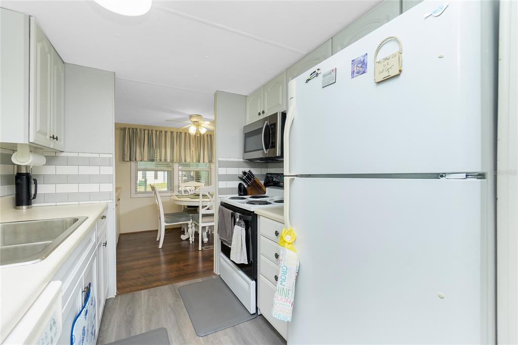 A galley kitchen with white cabinets and stainless steel appliances opens into a dining area — 7598 RATAN CIRCLE, PORT CHARLOTTE, FL