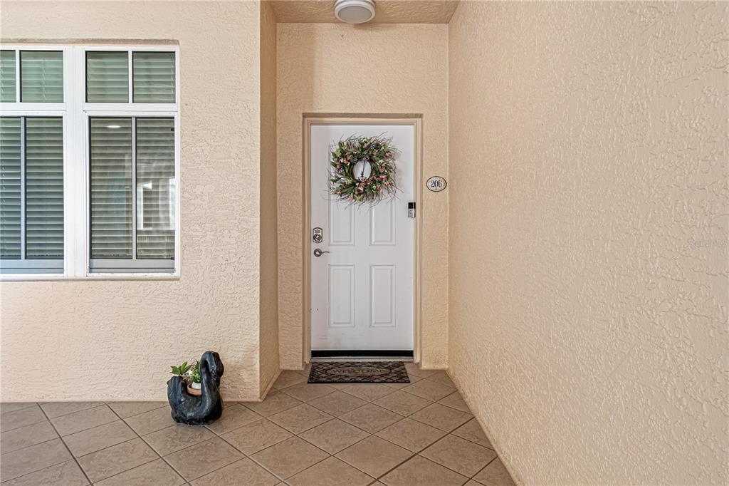 A white front door with a wreath and a swan statue sits on a tiled porch — 263 MINORCA BEACH WAY UNIT 206, NEW SMYRNA BEACH, FL