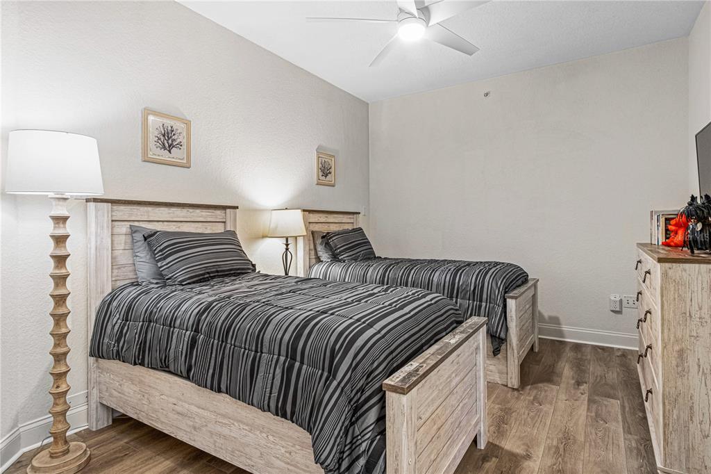 A bedroom features two twin beds with striped bedding, wood-look flooring, and a ceiling fan — 263 MINORCA BEACH WAY UNIT 206, NEW SMYRNA BEACH, FL