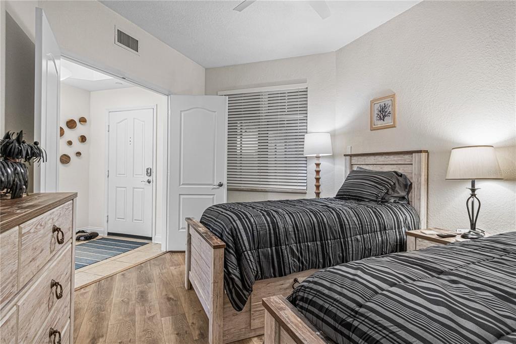 A bedroom features two twin beds with striped bedding, wood-look flooring, and a white door — 263 MINORCA BEACH WAY UNIT 206, NEW SMYRNA BEACH, FL