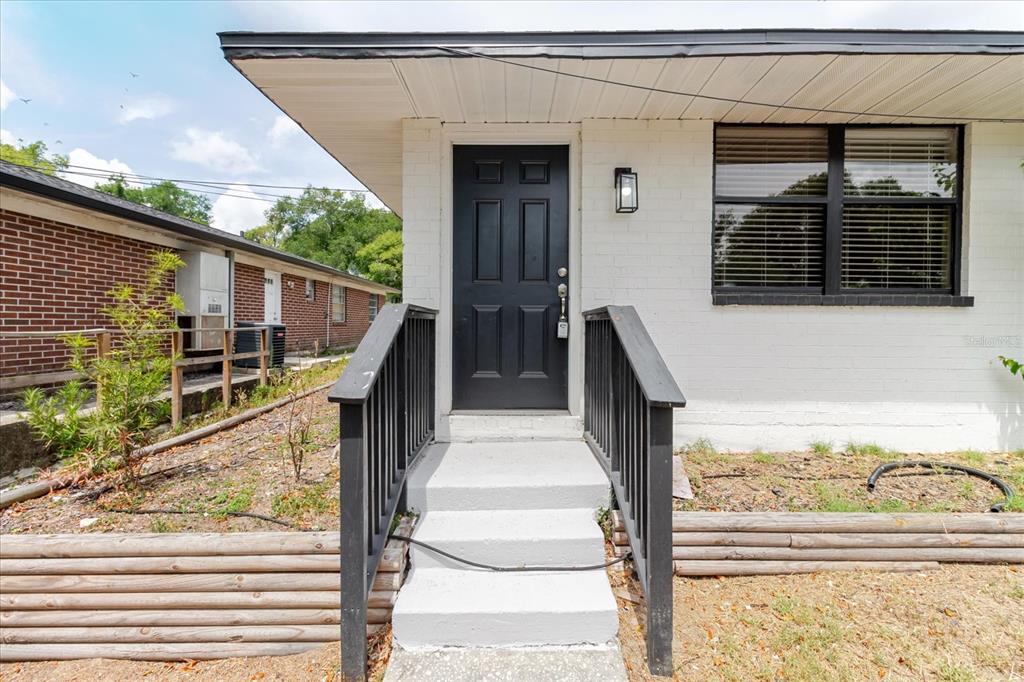 A white brick house exterior features a black front door, concrete steps, and black railings — 1134-1136 GILMORE AVENUE, LAKELAND, FL
