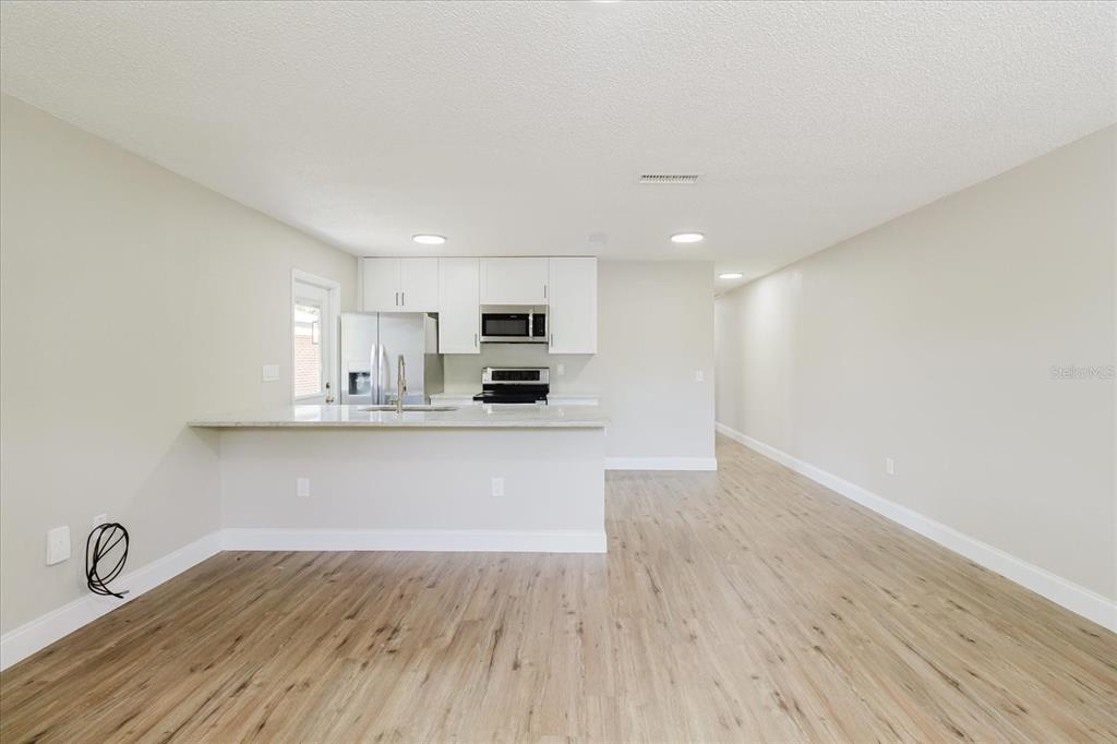 An open-concept kitchen features white cabinets, stainless steel appliances, and light wood-look flooring — 1134-1136 GILMORE AVENUE, LAKELAND, FL
