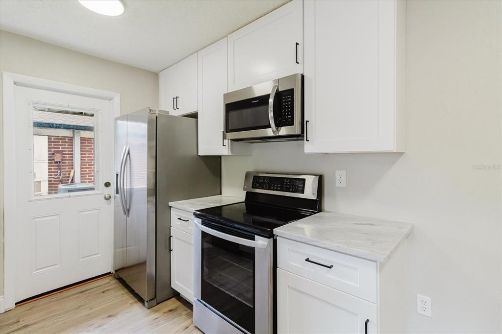 A kitchen features white cabinets, stainless steel appliances, and light-colored countertops — 1134-1136 GILMORE AVENUE, LAKELAND, FL