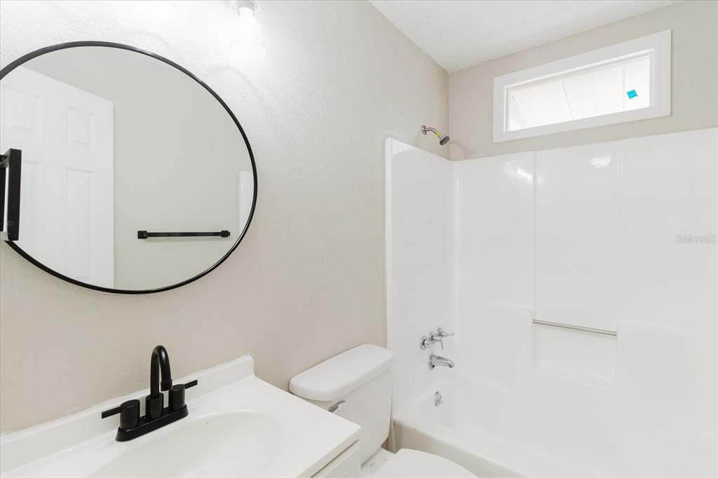 A bathroom features a white vanity with a black faucet, round mirror, and tub-shower combo — 1134-1136 GILMORE AVENUE, LAKELAND, FL