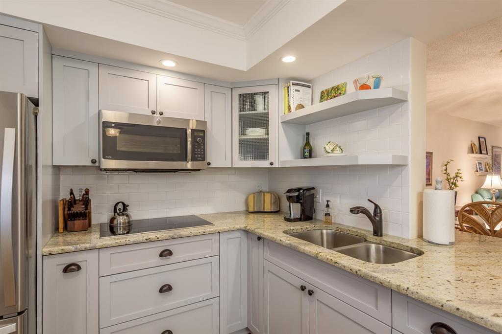 A kitchen features light gray cabinets, granite countertops, a stainless steel microwave, and open shelving — 952 VIRGINIA STREET UNIT 105, DUNEDIN, FL