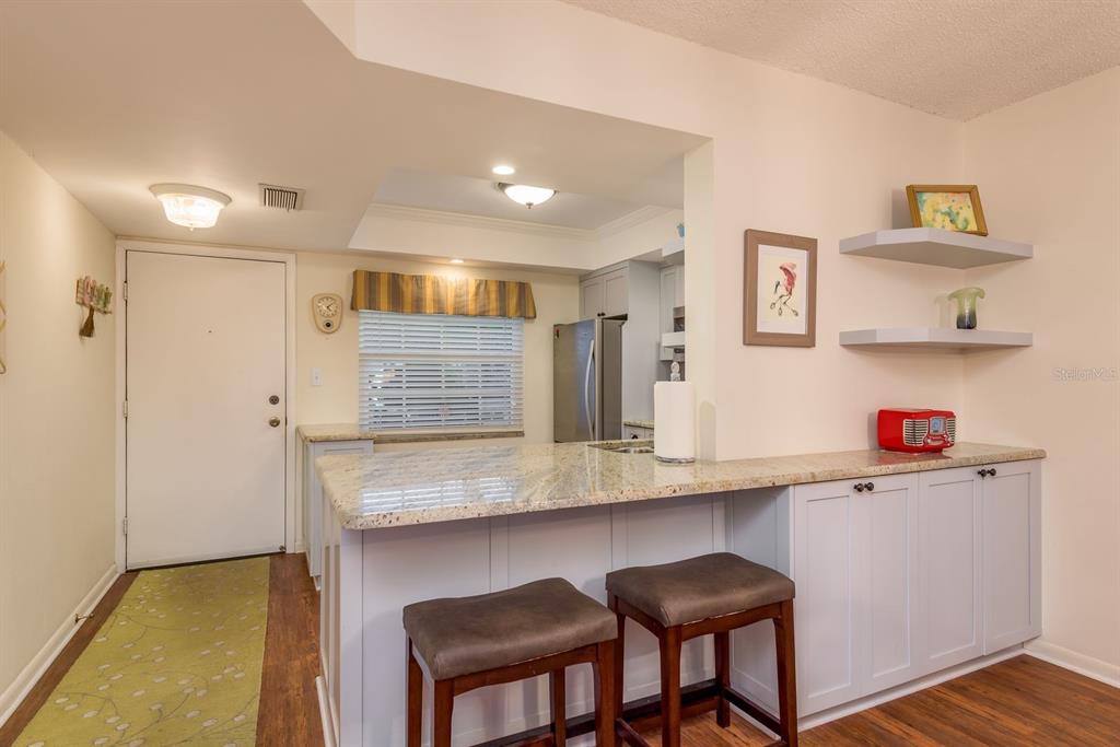 A kitchen features a granite breakfast bar, light blue cabinets, and two dark stools — 952 VIRGINIA STREET UNIT 105, DUNEDIN, FL