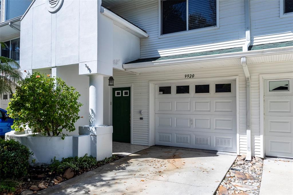A white house exterior features a green front door, a garage, and a small garden — 9920 INDIAN KEY TRAIL UNIT 29, SEMINOLE, FL