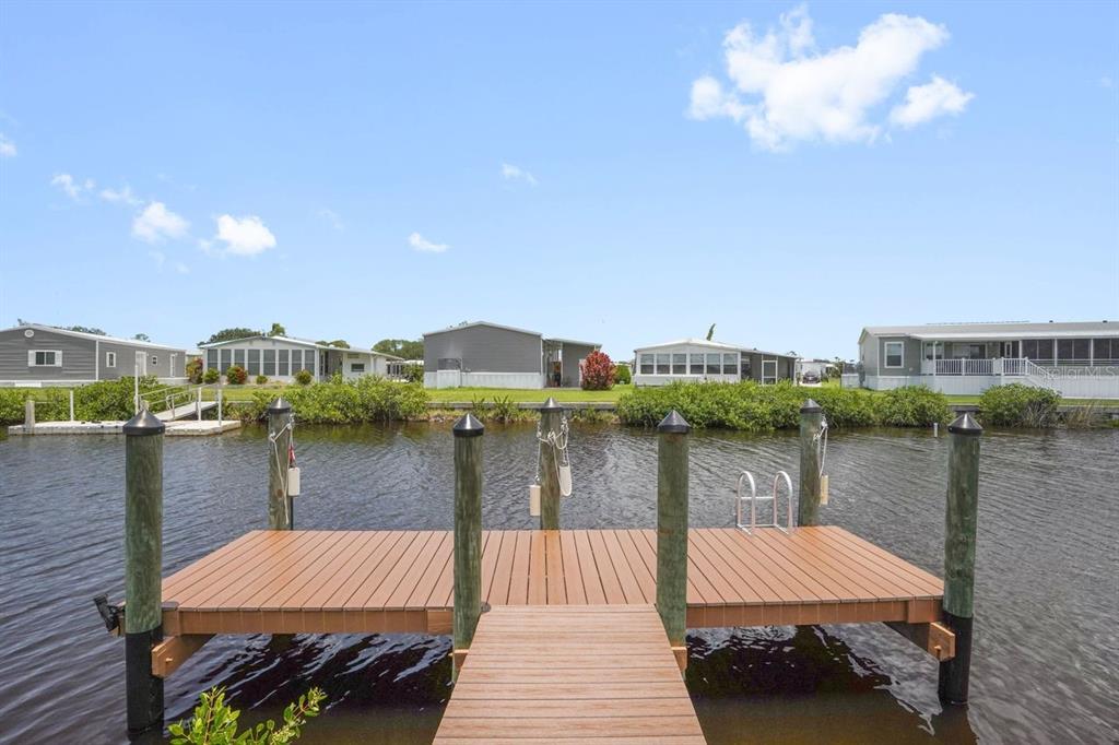 A wooden dock extends into a canal with several manufactured homes visible in the background — 654 BLACKBURN BOULEVARD, NORTH PORT, FL