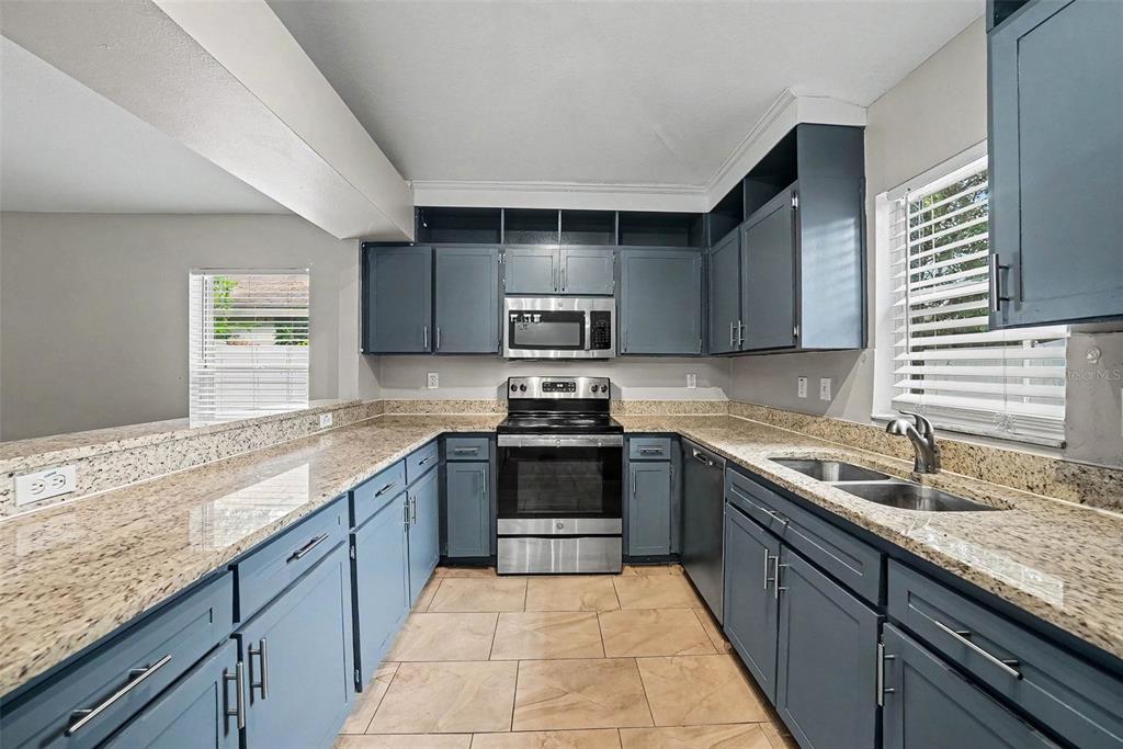 A kitchen features blue cabinets, granite countertops, stainless steel appliances, and beige tile flooring — 4803 DUNQUIN PLACE, TAMPA, FL
