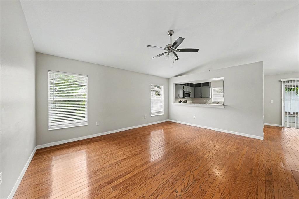 An empty living room features hardwood floors, a ceiling fan, and a kitchen pass-through window — 4803 DUNQUIN PLACE, TAMPA, FL