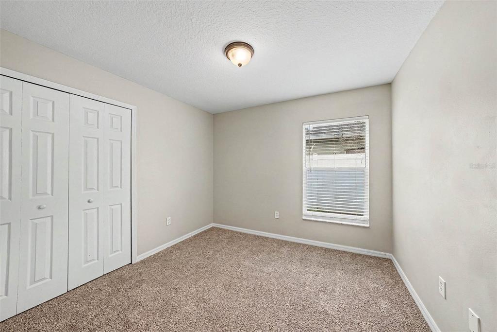 An empty bedroom features beige walls, tan carpeting, a white closet, and a single window — 4803 DUNQUIN PLACE, TAMPA, FL