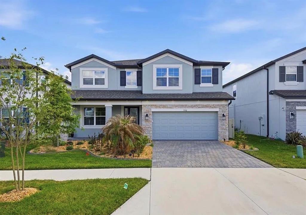 A two-story suburban house with light blue siding, a stone facade, and a two-car garage — 7792 NOTCHED PINE BEND, WESLEY CHAPEL, FL