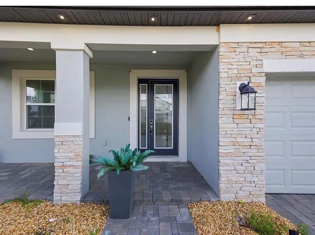A front entryway features a dark glass door, stone veneer accents, and a paved porch — 7792 NOTCHED PINE BEND, WESLEY CHAPEL, FL