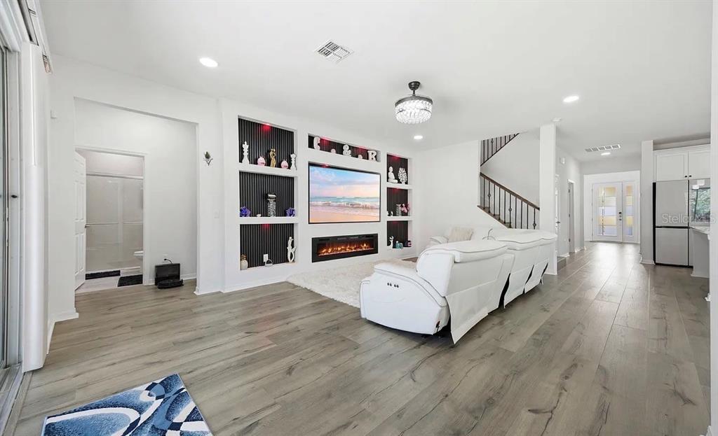 A living room with white walls, wood-look flooring, a fireplace, and a built-in media wall — 7792 NOTCHED PINE BEND, WESLEY CHAPEL, FL