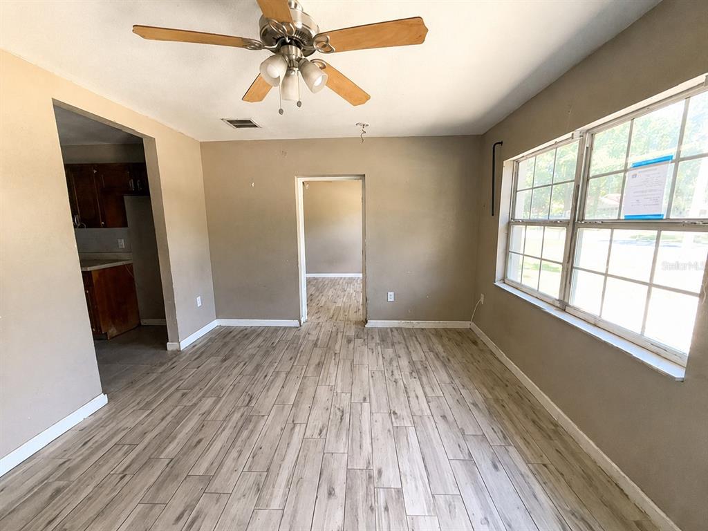 An empty room features light wood-look flooring, tan walls, a ceiling fan, and large windows — 508 OAKLAND ROAD, AUBURNDALE, FL