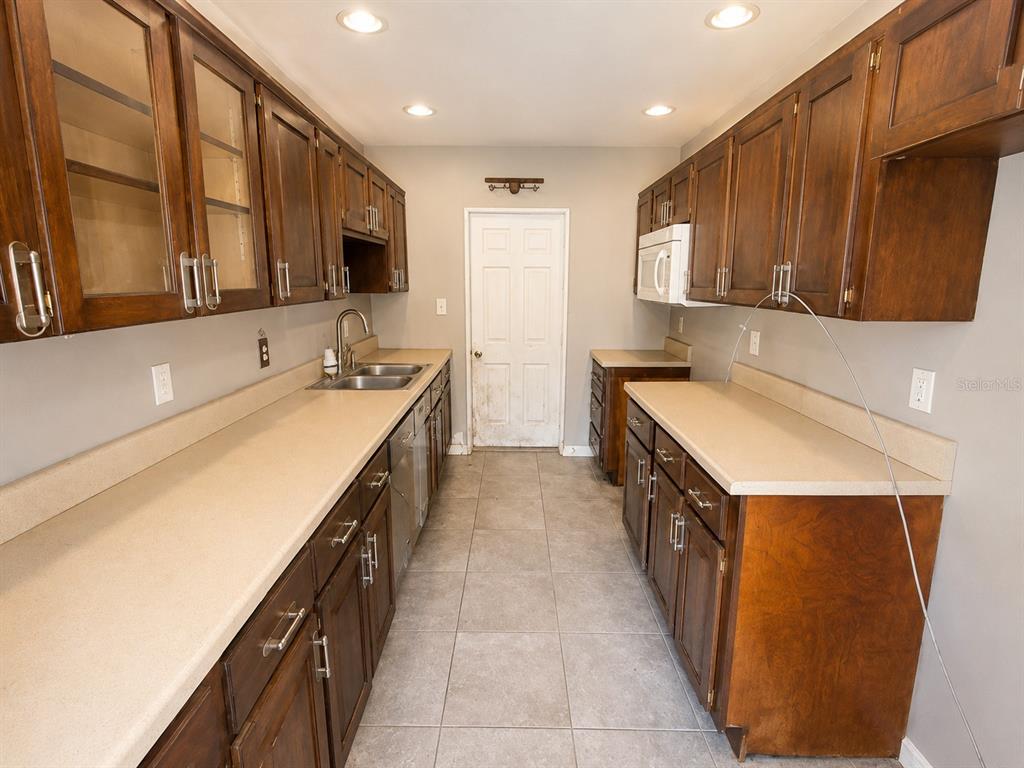 A galley kitchen features dark wood cabinets, beige countertops, and light-colored tile flooring — 508 OAKLAND ROAD, AUBURNDALE, FL