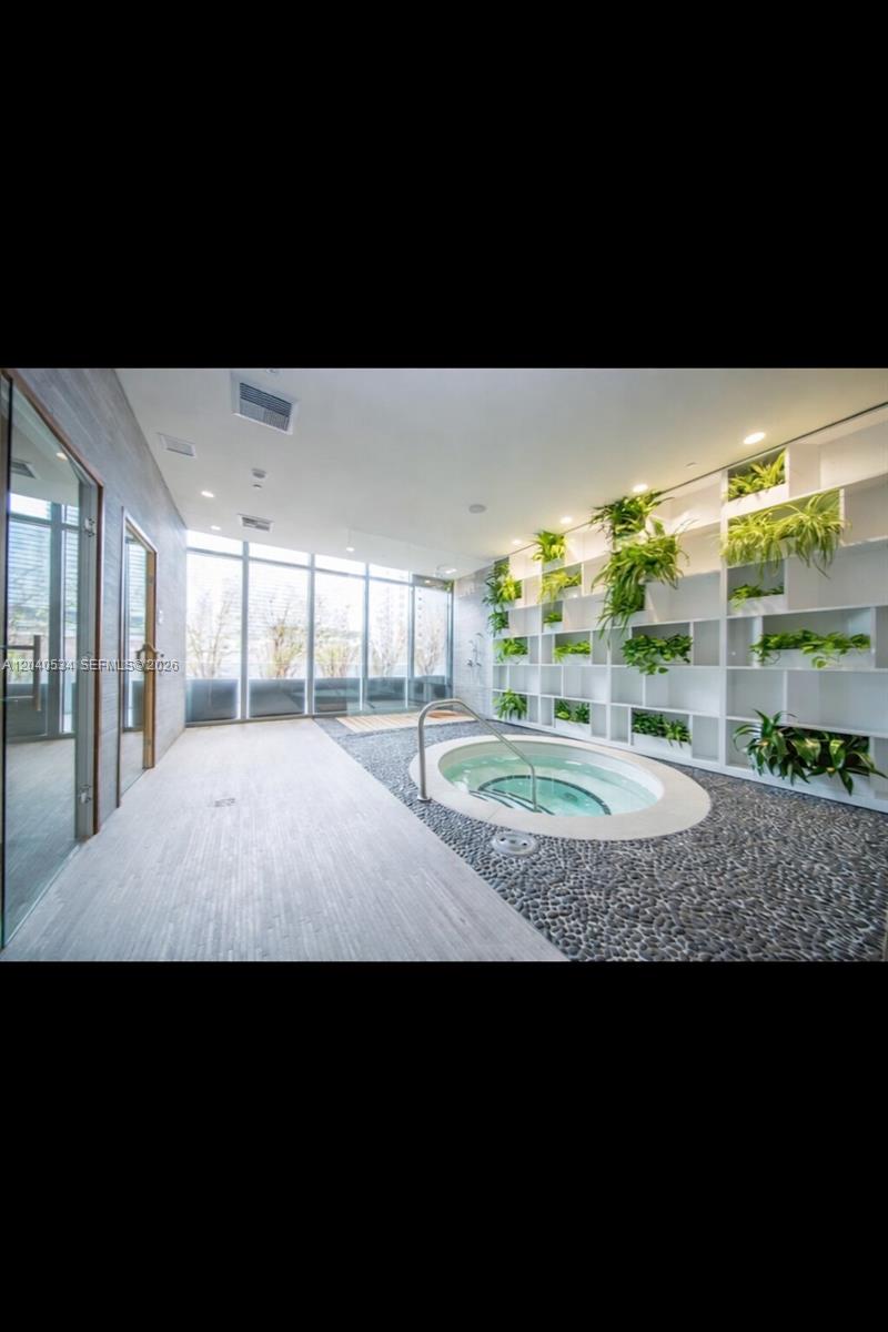 A spa room features a circular hot tub surrounded by river stones and a plant-filled shelving unit — 45 SW 9th St # 1004, Miami FL 33130, MIAMI, FL