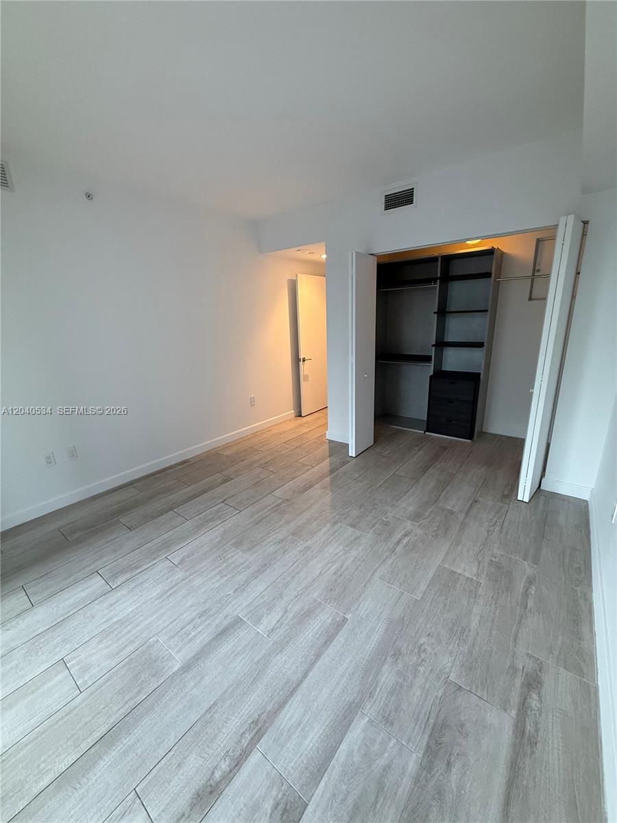 A bedroom features light wood-look tile flooring, white walls, and a built-in closet system — 45 SW 9th St # 1004, Miami FL 33130, MIAMI, FL