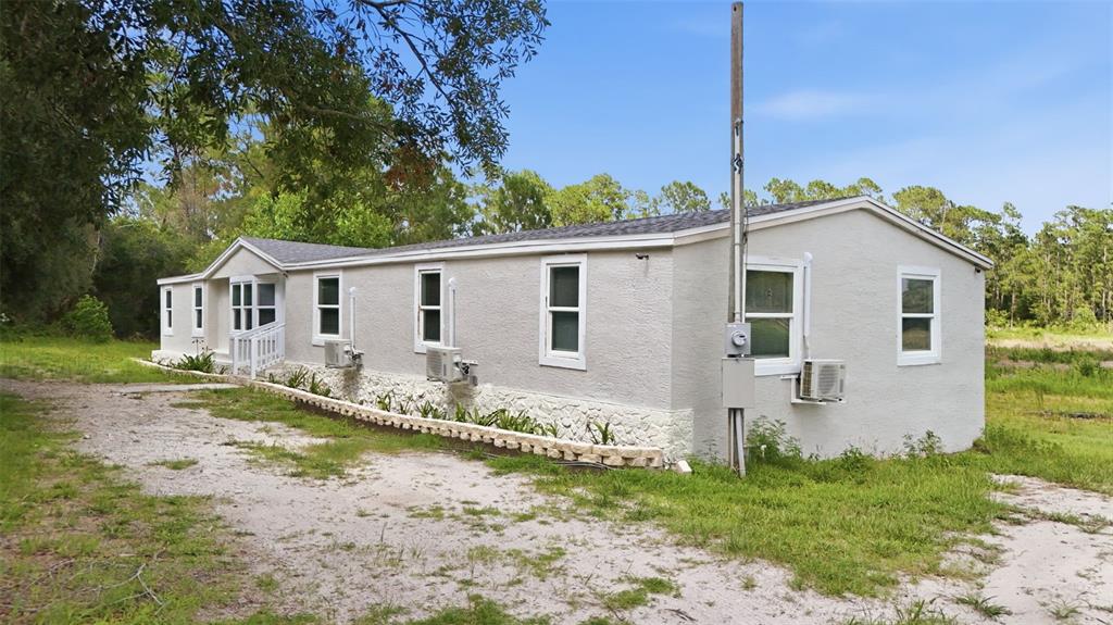 A light-colored single-story house with a stone-textured base sits on a dirt lot — 40404 HOLLY BRANCH ROAD, EUSTIS, FL