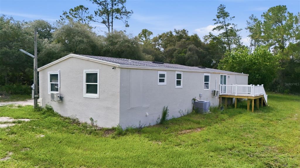 A single-story mobile home with a light-colored exterior and a small wooden deck — 40404 HOLLY BRANCH ROAD, EUSTIS, FL