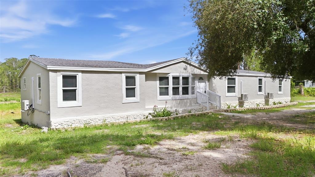 A single-story manufactured home with light-colored siding and a stone-textured foundation sits on a lot — 40404 HOLLY BRANCH ROAD, EUSTIS, FL