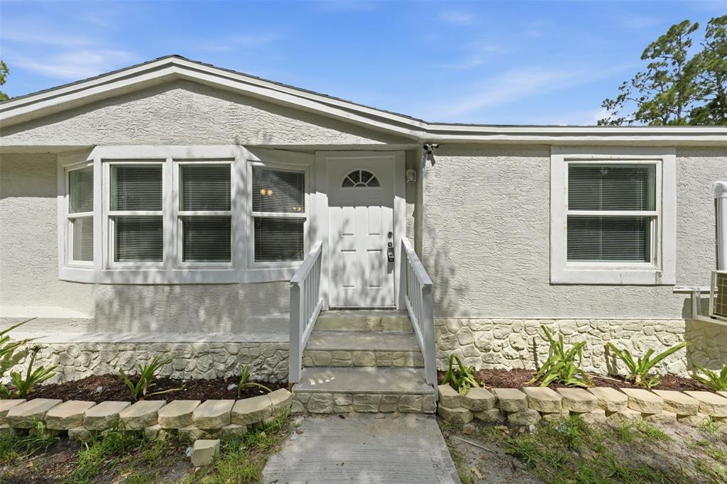 The exterior of a single-story home features a white door, bay windows, and stone skirting — 40404 HOLLY BRANCH ROAD, EUSTIS, FL