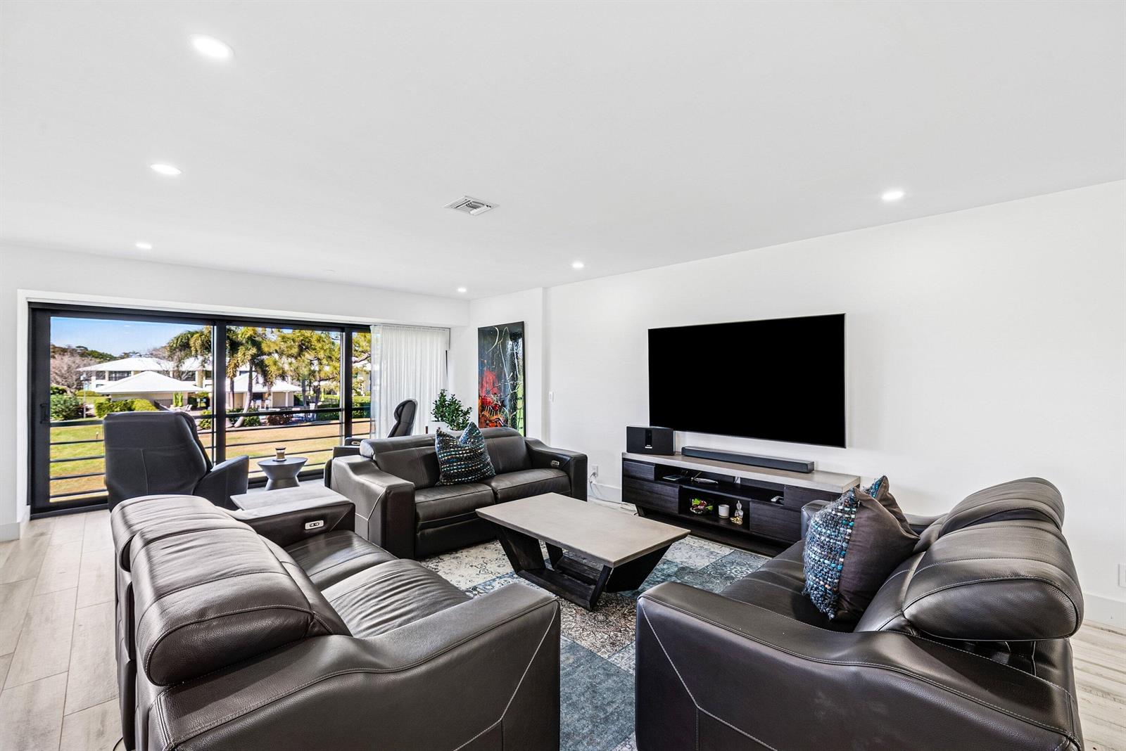 A living room features dark leather sofas, a television, and a sliding glass door view — 3667 Quail Ridge Drive N # B, Boynton Beach FL 33436, BOYNTON BEACH, FL